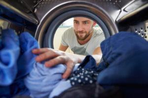 Mann, der Wäsche wäscht und in die Waschmaschine greift