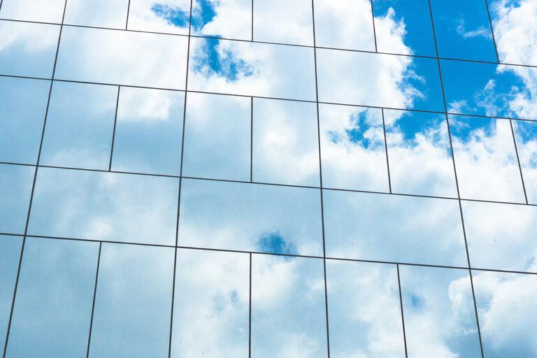 Blauer Himmel Reflexion in Glasfassade des Gebäudes. Blick auf Bürogebäude Fenster Nahaufnahme, Reflexion und Perspektive. Glasfassade an einem sonnigen Tag mit Sonnenstrahlen auf den blauen Himmel.