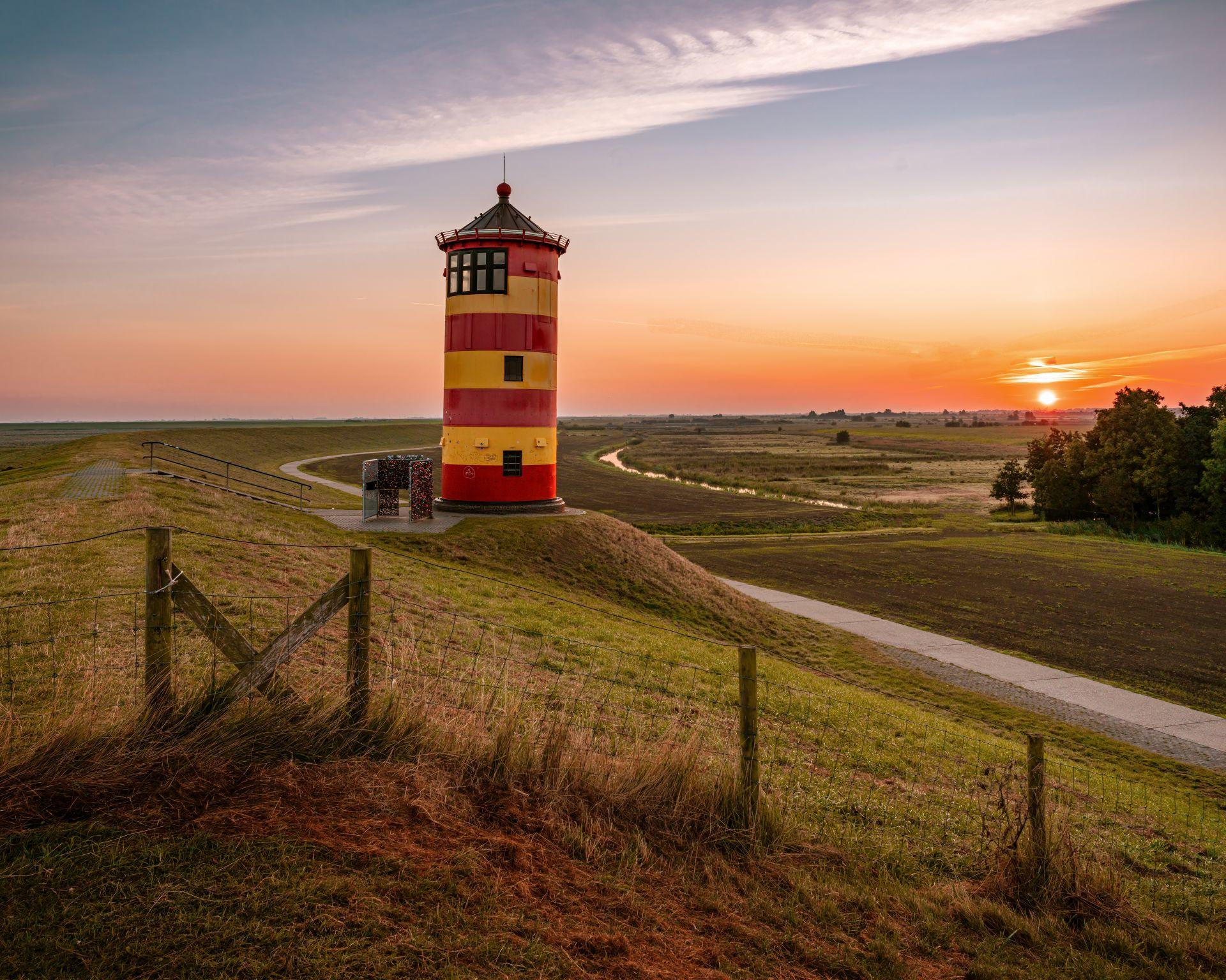 Leuchtturm an der Nordseekueste bei Sonnenuntergang mit Deich und Weitblick – Symbol fuer Sicherheit und Weitblick beim Hauskauf