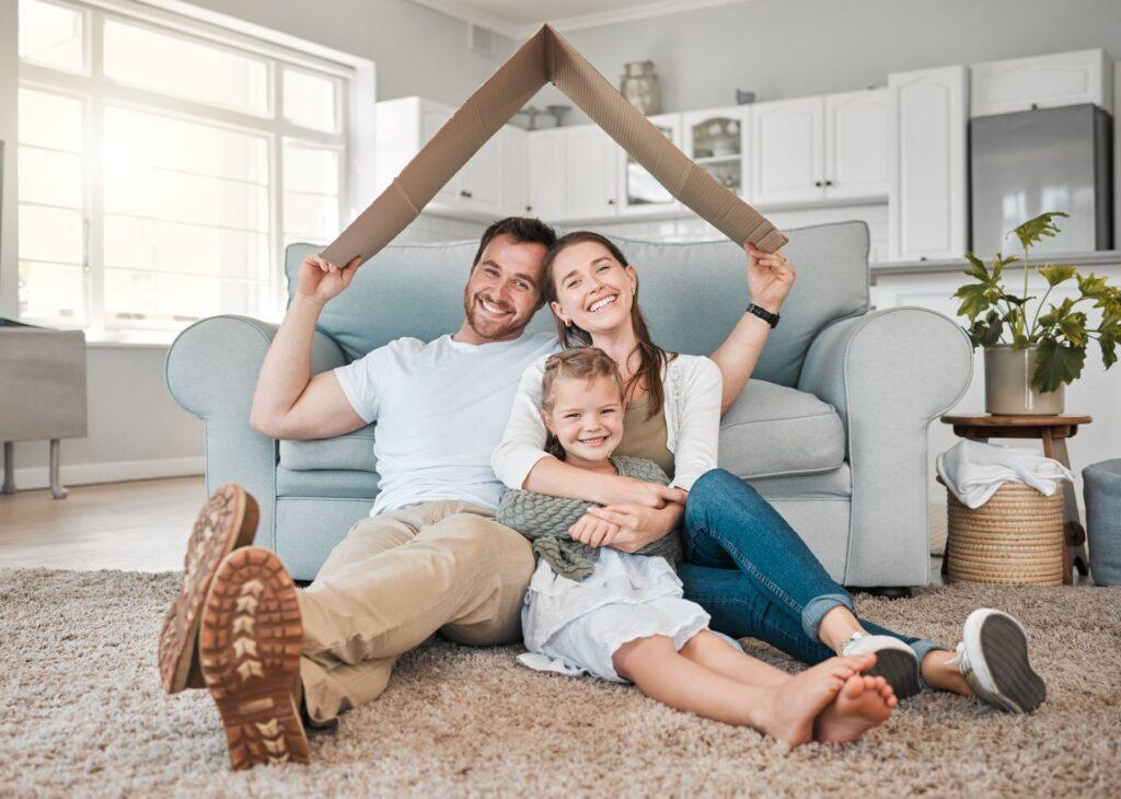 glueckliche familie mit kind unter kartondach auf sofa im neuen zuhause