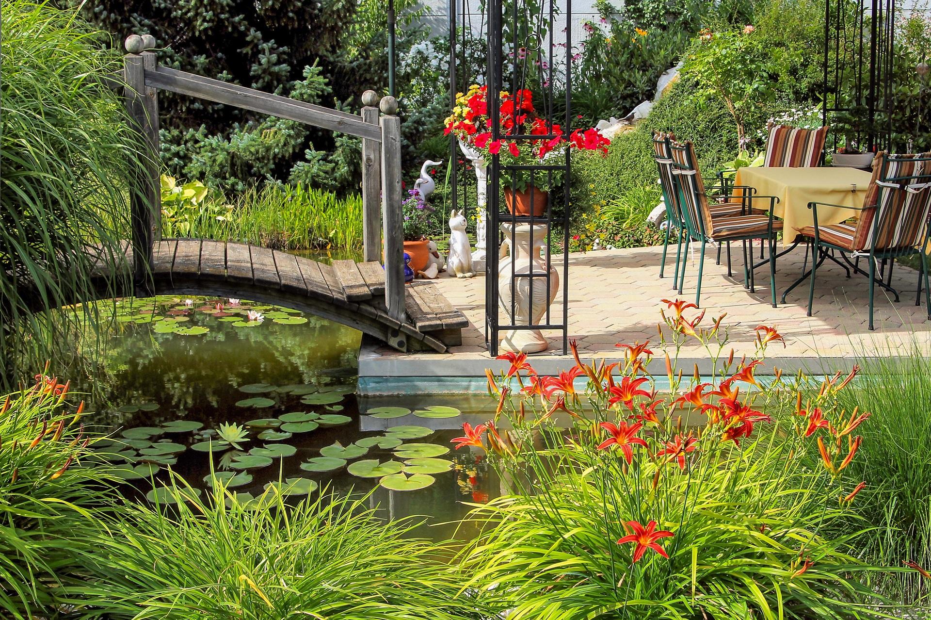 Teich mit Brücke und Gartenmöbeln | wasserdurchlässige Sonnensegel

