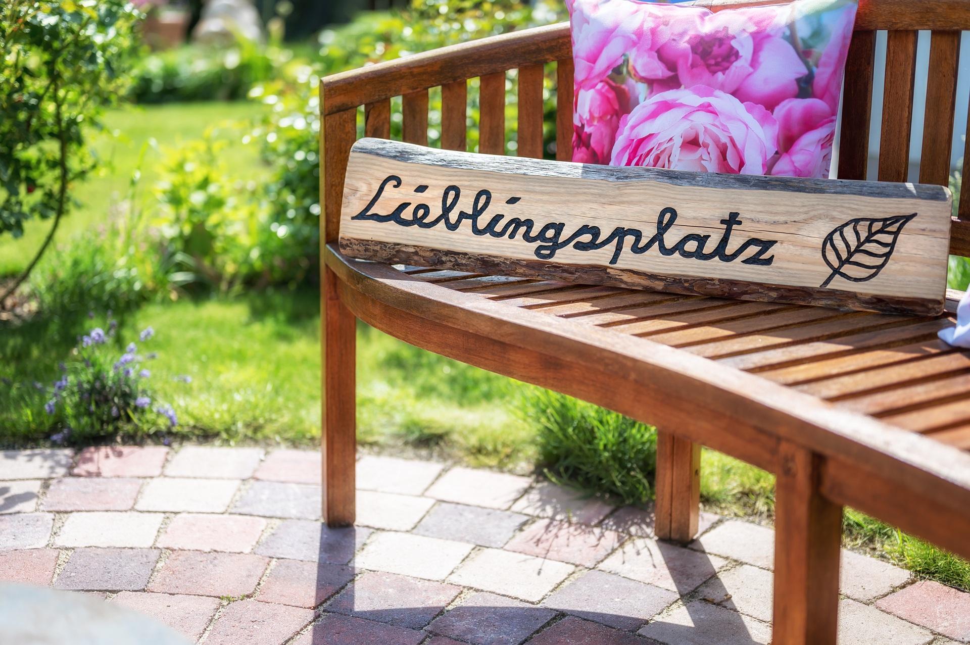 Gartenbank mit Lieblingsplatz-Schild auf Terrasse | wasserdurchlässige Sonnensegel

