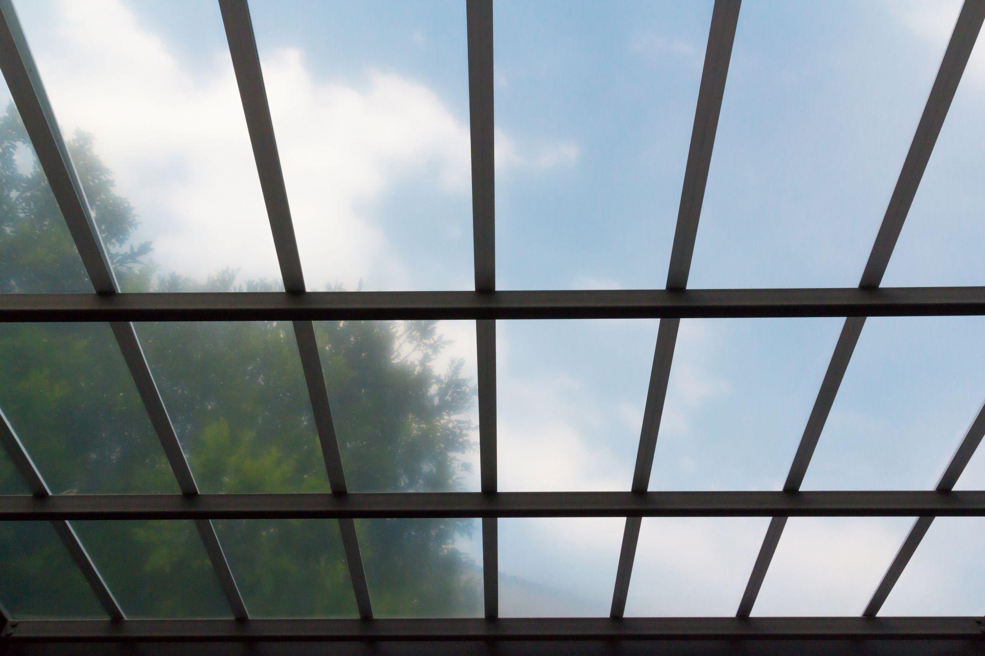 Klares Stegplattendach mit Metallrahmen von unten vor blauem Himmel – Beispiel fuer moderne Terrassenueberdachung